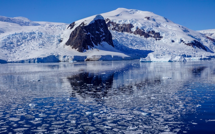 And Ice covered mountain in Antarctic is reflected perfectly like a mirror in the royal blue water speckled with ice