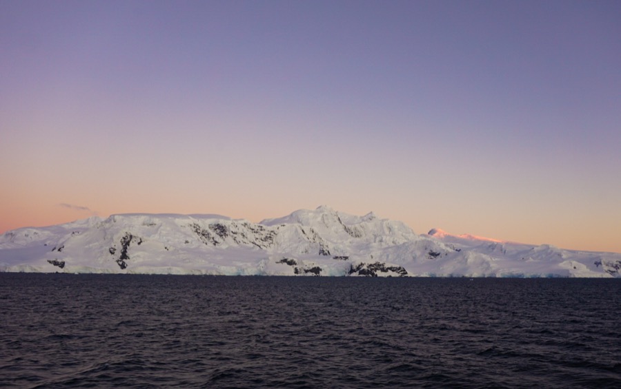 Sunrise over an icy mountain in Antarctica. The sky is pink and purple behind the white mountain.