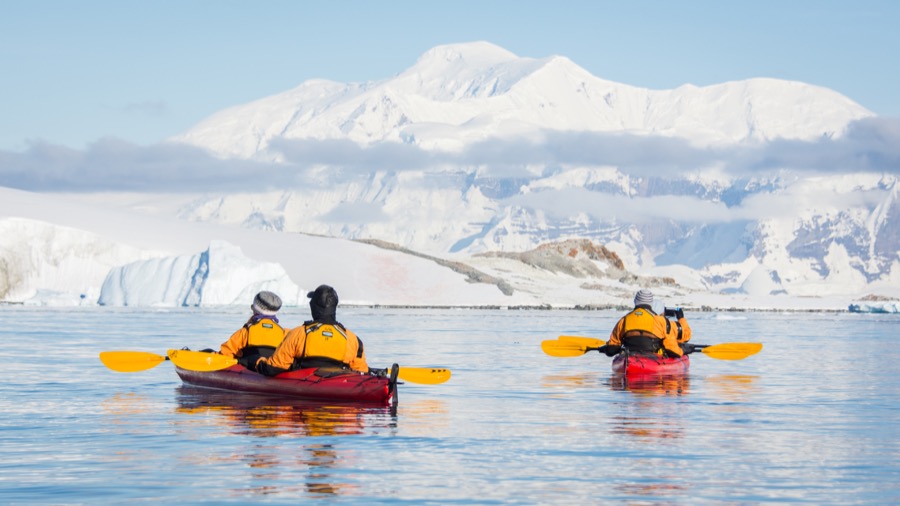Kayakers on crystal clear water surrounding by white mountains in Antarctica