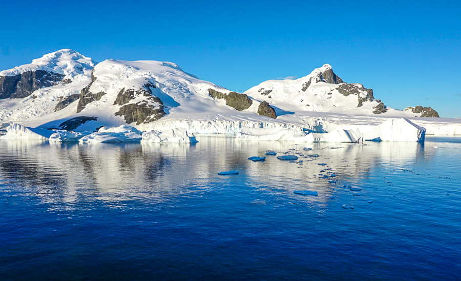 Icy Mountains reflected in blue glass waters in ANtarctica